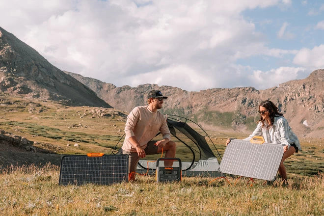 Jackery Explorer 1000 Pro gekoppeld aan draagbare zonnepanelen naast twee kamperende mensen met een tent