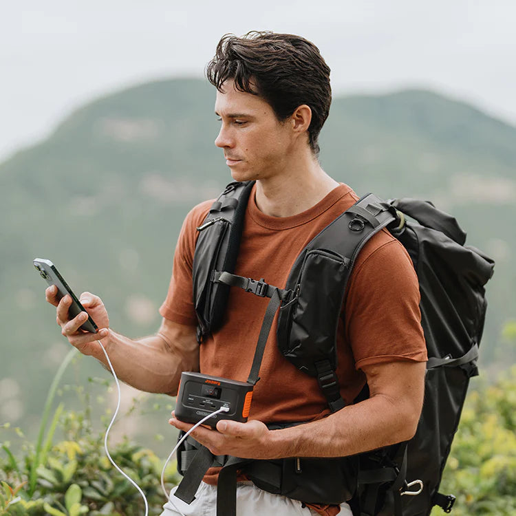 Jackery Explorer 100 Plus powerbank voorziet een smartphone van stroom in de handen van een backpacker